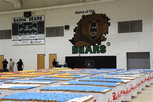 Image of doughnuts on rows of tables in a gym. Home of the Basha Bears logo on wall